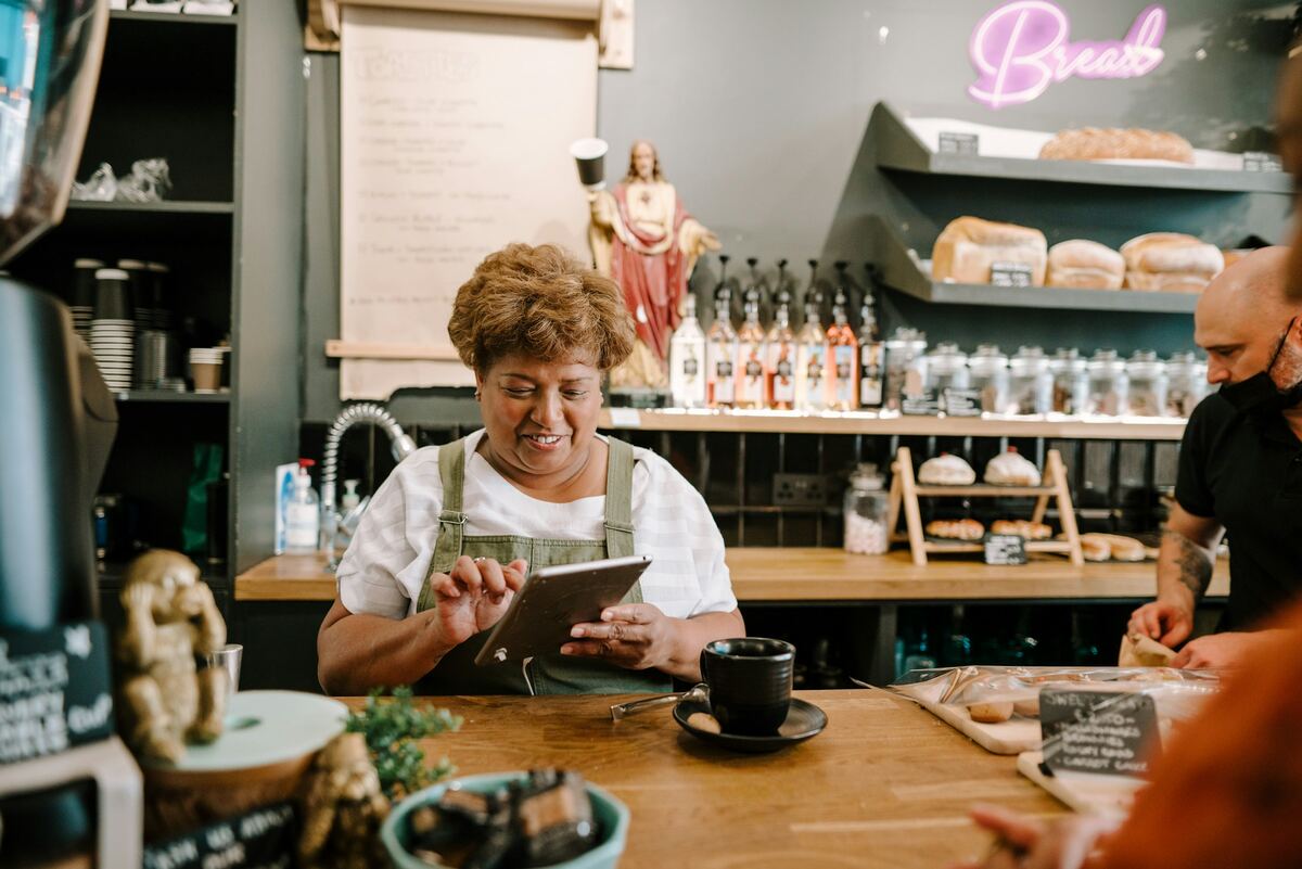 A smiling cafe owner using a tablet at the counter